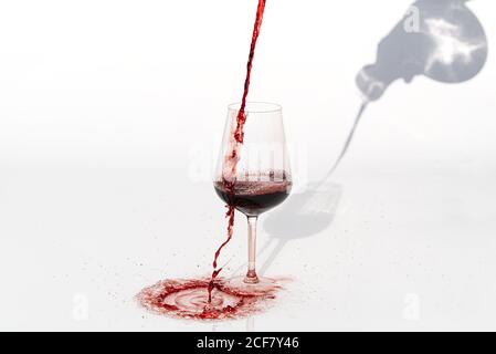 Sommelier gießt Rotwein von Dekanter zu Weinglas auf weißem Hintergrund. Verschüttet Rotwein am Glas vorbei auf einem weißen Tisch. Stockfoto