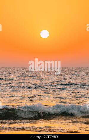 Sonnenuntergang Sonne Glanz Über Meer. Natürlicher Sonnenaufgang Himmel Warme Farben Über Dem Wellenmeer. Meerwasser Schaum Spritzer Waschen Sandstrand Stockfoto