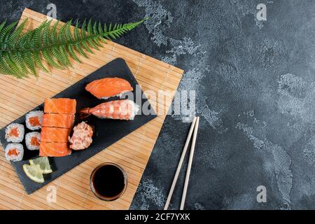 Sashimi rollt auf einem schwarzen Stein slatter. Nahaufnahme des Sushi-Sets mit Essstäbchen und Soja Stockfoto