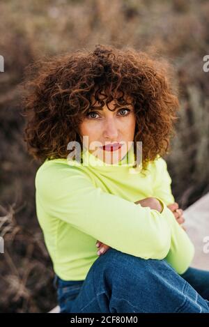 Von oben von jungen weiblichen Modell in trendigen Casual Wear Und Brillen mit roten Lippen sitzen auf Stein und schauen Bei der Kamera Stockfoto