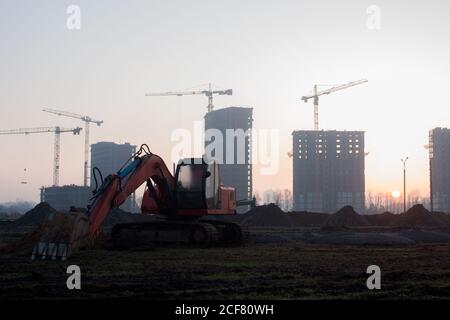 Bagger auf der Baustelle auf dem Hintergrund eines Baukräne und Gebäude. Graben Sie den Boden für das Fundament, Verlegung Sturm Kanalisation Rohre. Sma Stockfoto