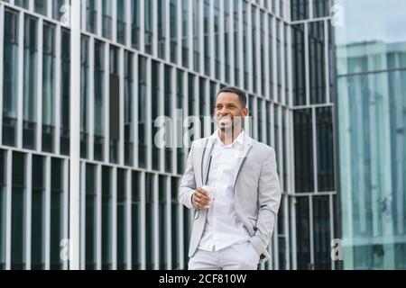 Eleganter afroamerikanischer Geschäftsmann, der Kaffee hält und sich anschaut Business Center im Stadtzentrum Stockfoto