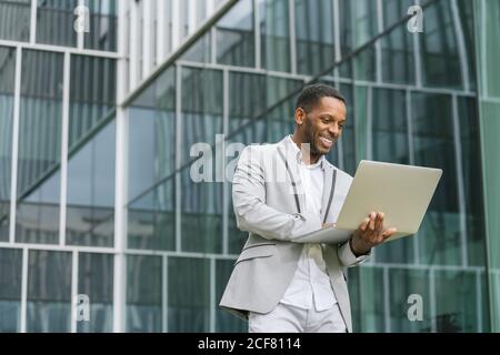 Modisch lächelnd afroamerikanischen Geschäftsmann hält Laptop und arbeiten tippen Auf der Tastatur im Hintergrund des Business Centers Stockfoto