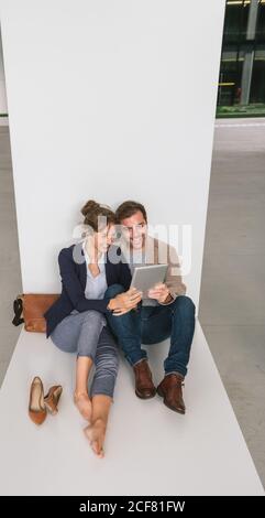 Fröhliche Paar umarmen einander beim Surfen auf einem Tablet Sitzen Sie vor einem modernen Gebäude an einer Stadtstraße zusammen Stockfoto