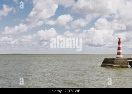 Gestreifter Leuchtturm am Ufer des Meeres an einem bewölkten Tag Stockfoto