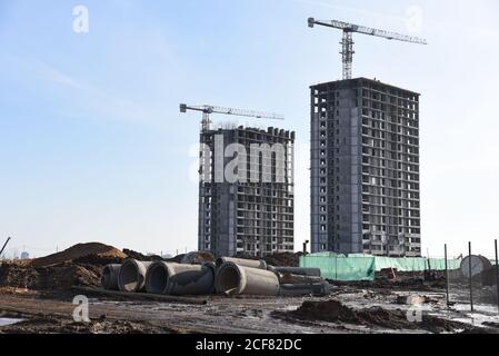 Turmdrehkrane arbeiten auf der Baustelle auf blauem Himmel Hintergrund. Verlegung von Betonschächten und Abflussrohren für das Regenwassersystem. Regenwasser aufbauen Stockfoto