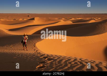 Unerkennbarer Reisender, der auf Sand steht und dabei Dünen fotografiert In einer unglaublichen Wüste Stockfoto