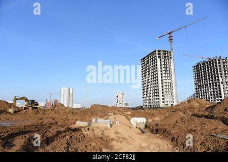 Bagger am Gebäude im Bau. Bagger gräbt den Boden für das Fundament und für die Verlegung von Kanalrohren. Renovierungsprogramm. Gebäude industr Stockfoto