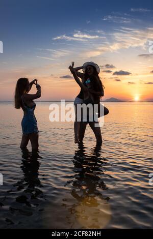 Glückliche Freundinnen, die beim Sonnenuntergang am Meer dummten und Fotos machten Im Sommer Stockfoto