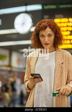 Rothaarige junge Frau mit Smartphone am Bahnhof Stockfoto