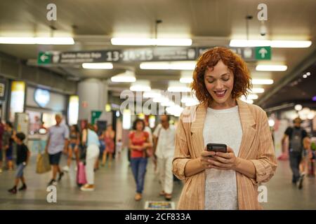 Rothaarige junge Frau mit Smartphone am Bahnhof Stockfoto