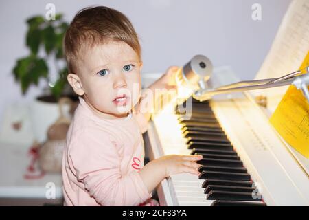 Kleines Mädchen spielt zum ersten Mal gerne E-Piano (Synthesizer). Kleine Kinder spielen den Klaviersynthesizer zu Hause mit Klaviernoten Stockfoto