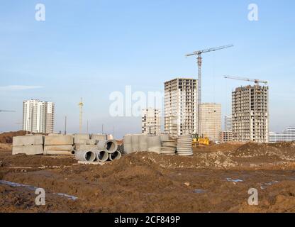 Turmdrehkrane arbeiten auf der Baustelle auf blauem Himmel Hintergrund. Verlegung von Betonschächten und Abflussrohren für das Regenwassersystem. Regenwasser aufbauen Stockfoto