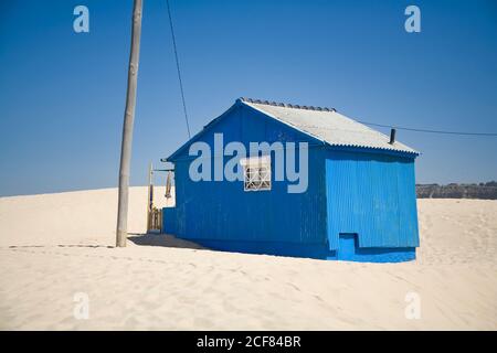 Kleines blaues Haus mit schäbigen Wänden am sandigen Meer gelegen Mit blauem Himmel im Hintergrund an sonnigen Tagen Stockfoto