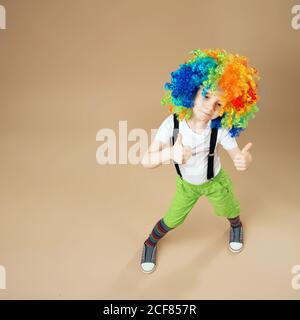 Blithesome Kinder. Fröhlicher Clownsjunge mit großer bunter Perücke. Kleiner Junge in Clown Perücke tanzen und Spaß haben. Porträt eines Kindes auf einem Weitwinkel aufgenommen Stockfoto