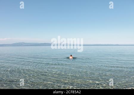 Rückansicht des gebräunten Mannes, der ruhiges klares Wasser genießt, das friedlich in hellen sonnigen Tag schwimmt, Chalkidiki, Griechenland Stockfoto