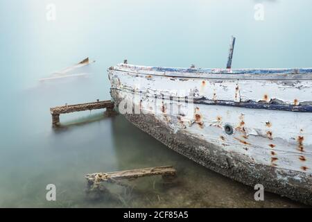Stilles Meerwasser mit altem rostigen Boot, das auf der Küste im Nebel liegt, Chalkidiki, Griechenland Stockfoto