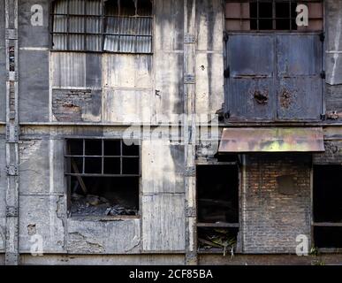 Außenansicht eines verlassenen Industriegebäudes aus Stein mit schmalen Fenstern mit Metallgitter und zerbrochenes Glas Stockfoto