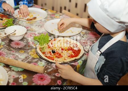 Kinder machen Pizza. Meisterkurs für Kinder zum Kochen italienischer Pizza. Kleine Kinder lernen, eine Pizza zu kochen. Kinder bereiten hausgemachte Pizza. Kleines c Stockfoto