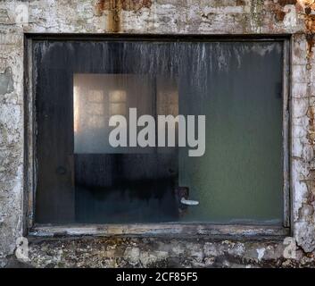 Fragment der verwitterten Steinwand mit kleinen schmutzigen Fenster Verkommen Industriegebäude Stockfoto