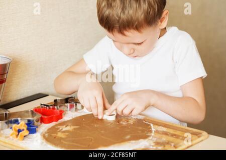 Kinderhände machen Lebkuchen. Kleiner Junge, der Cookies zu Weihnachten schneidet. Kind Backen Kochen Cookies Spaß Konzept. Meisterkurs für Kinder auf bakin Stockfoto