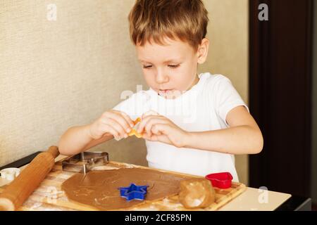 Kinderhände machen Lebkuchen. Kleiner Junge, der Cookies zu Weihnachten schneidet. Kind Backen Kochen Cookies Spaß Konzept. Meisterkurs für Kinder auf bakin Stockfoto