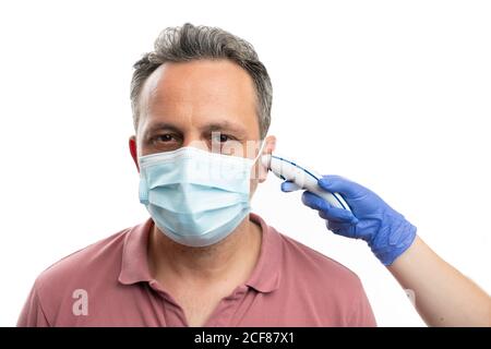 Mann trägt OP-Maske mit Temperatur im Ohr gemessen mit Laserthermometer von Person, die medizinische Latexhandschuhe als covid19 trägt Symptomkonzept Stockfoto