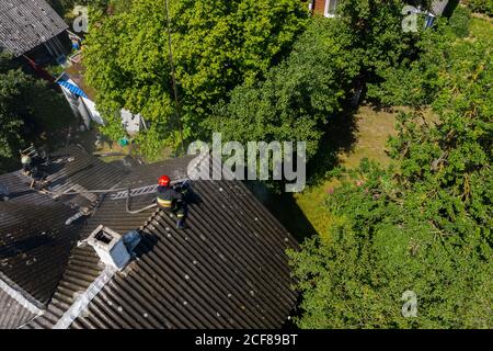 Ein Feuerwehrmann sitzt auf dem Dach eines brennenden Hauses. Stockfoto