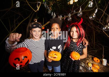 Porträt von glücklichen Kindern in Halloween-Kostüme halten Kürbisse und Lächelnd auf die Kamera, während sie im Dunkeln steht Stockfoto