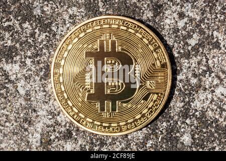 Bitcoin-Logo, runde Kryptomünze aus Metall Gold, repräsentatives Kryptowährungssymbol auf konkretem Hintergrund, Nahaufnahme. Münze liegt auf dem Boden Stockfoto