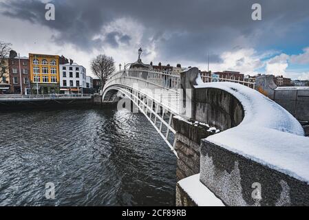 Dramatische Aussicht auf die Ha ' Penny Brücke von Schnee bedeckt gegen dichte Wolken. Die irische Überführung über den Fluss Liffey vermittelt ein Gefühl der Gemeinschaft Stockfoto