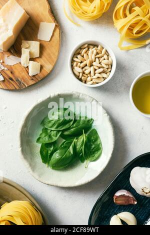 Draufsicht auf frische grüne Basilikumblätter auf dem Teller als nächstes Zu Pinienkernen und Parmesankäse auf weißem Küchentisch Stockfoto