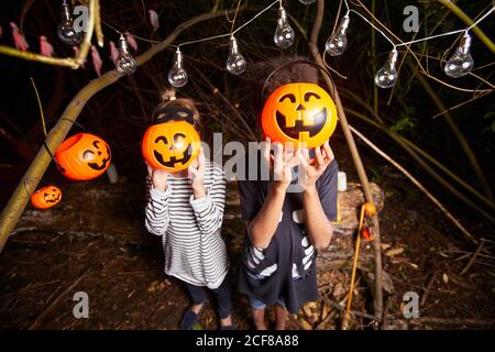 Porträt von zwei Kindern halten Spielzeug Kürbisse vor Ihre Gesichter, während sie an Halloween im Dunkeln stehen Party