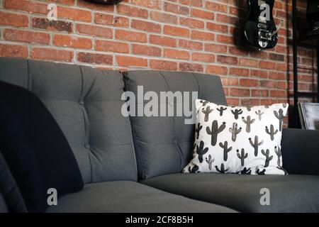 Sammlung von Gitarren und Banjos, die oben an der Ziegelwand hängen Gemütliches Sofa mit Kissen und Nachttisch beiseite in der Wohnung Stockfoto