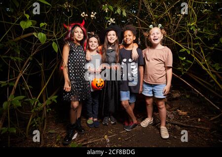 Portrait von glücklichen Kindern in Halloween Kostümen im Stehen Dunkler Wald und lächelnd an der Kamera Stockfoto