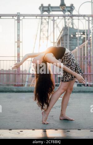 Seitenansicht der jungen anmutigen Tänzerin in casual Rock Ausführen Rückenbeuge beim Stehen barfuß auf Brücke in Rücken Leuchtet Stockfoto