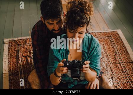 Von oben gesehen, wie ein Paar aus Hipster und Frau mit einer Fotokamera barfuß auf dem Wohnungsboden sitzt Stockfoto