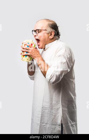 Bald Senior indischen asiatischen Mann essen Popcorn über weißem Hintergrund Mit fröhlichen Ausdrücken Stockfoto