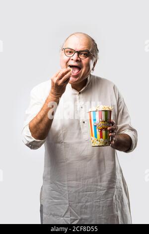 Bald Senior indischen asiatischen Mann essen Popcorn über weißem Hintergrund Mit fröhlichen Ausdrücken Stockfoto