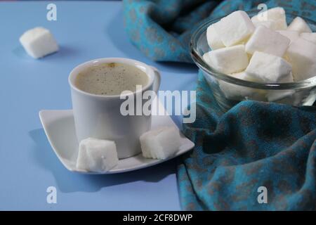 Stapel von weißen hausgemachten Marshmallows in einer transparenten Schüssel auf blauem Hintergrund. Tasse heißen Kaffee und hausgemachten Marshmallows. Food-Konzept. Stockfoto