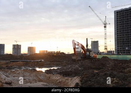 Großer Raupenbagger auf Baustelle im Hintergrund Sonnenuntergang. Bagger graben den Boden für das Fundament, Verlegung Sturm Kanalisation Rohre. Installation Stockfoto