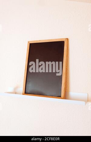 Leere Tafel mit braunem Holzrahmen auf weißem Regal gegen Hellbeigefarbene Wand im modernen Büro Stockfoto