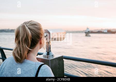 Rückansicht von anonymen weiblichen Reisenden im lässigen Outfit stehend Am Ufer und bewundernde Aussicht auf bunte erstaunliche Sonnenuntergang Stockfoto