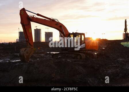 Großer Raupenbagger auf Baustelle im Hintergrund Sonnenuntergang. Bagger graben den Boden für das Fundament, Verlegung Sturm Kanalisation Rohre. Installation Stockfoto