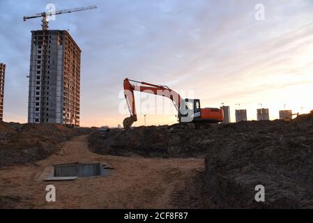 Großer Raupenbagger auf Baustelle im Hintergrund Sonnenuntergang. Bagger graben den Boden für das Fundament, Verlegung Sturm Kanalisation Rohre. Installation Stockfoto