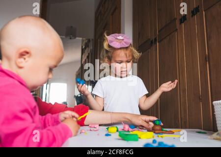 Nette fröhliche kleine Kinder in legerer Kleidung, die mit Plastilin spielt Während Sie zu Hause Zeit zusammen verbringen Stockfoto