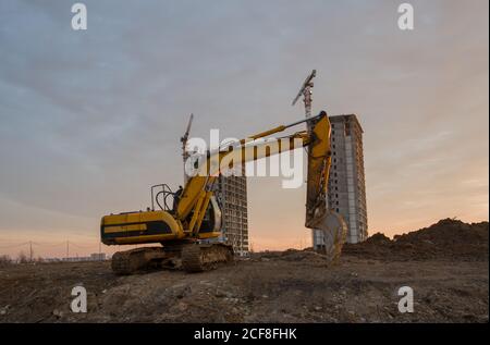 Großer Raupenbagger auf Baustelle im Hintergrund Sonnenuntergang. Bagger graben den Boden für das Fundament, Verlegung Sturm Kanalisation Rohre. Installation Stockfoto