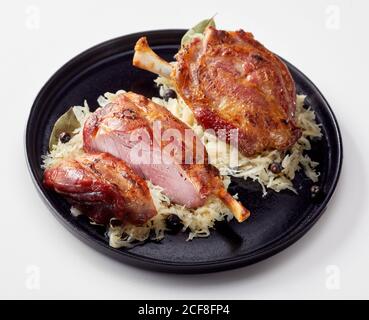 Doppelportion von traditionell geröstetem deutschen Eisbein oder Schweineschinken hock auf Sauerkraut serviert auf einem Teller über weiß Stockfoto