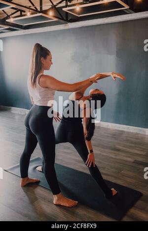 Lächelnd fleißig weibliche Ausbilderin Sportswear Lehre drehten Dreieck Pose Für eine Gruppe von sportlichen Menschen, die auf der Übung stehen Sportmatten im modernen Fitnessraum Stockfoto