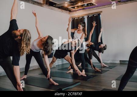 Lächelnd fleißig weibliche Ausbilderin Sportswear Lehre drehten Dreieck Pose Für eine Gruppe von sportlichen Menschen, die auf der Übung stehen Sportmatten im modernen Fitnessraum Stockfoto